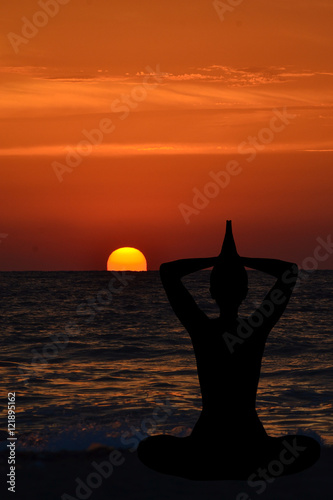 Silhouette of young woman practicing yoga on the beach at sunris