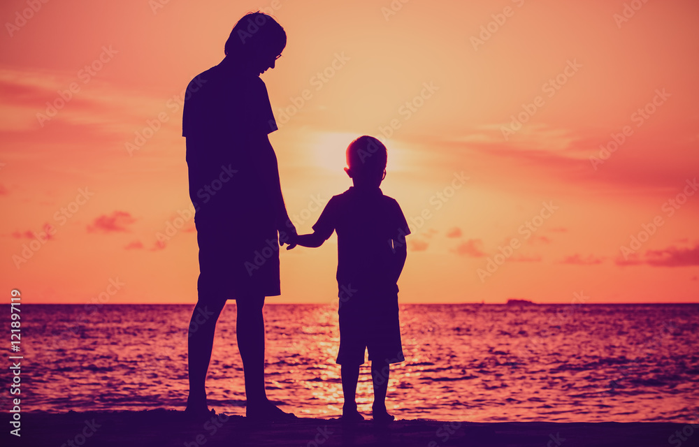 silhouette of father and son holding hands at sunset sea