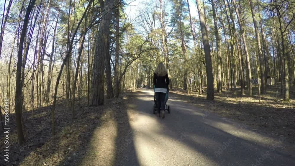 Mother push baby pushchair in spring park path. 4K