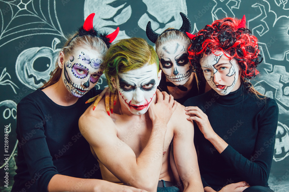 Fototapeta premium Three girls and a guy with Halloween face art on dark background pattern