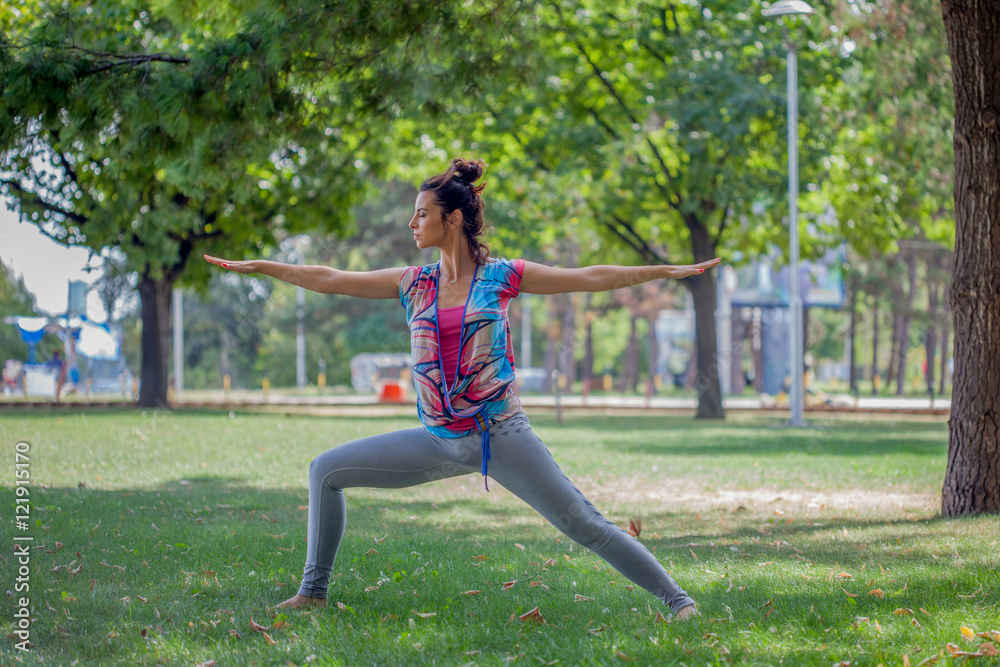 Young woman practicing yoga in the park on the green grass with