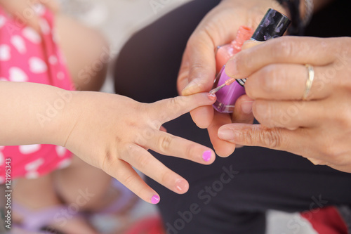 Woman applying nail polish, doing manicure to a little girl, fun activity at home or girl birthday party