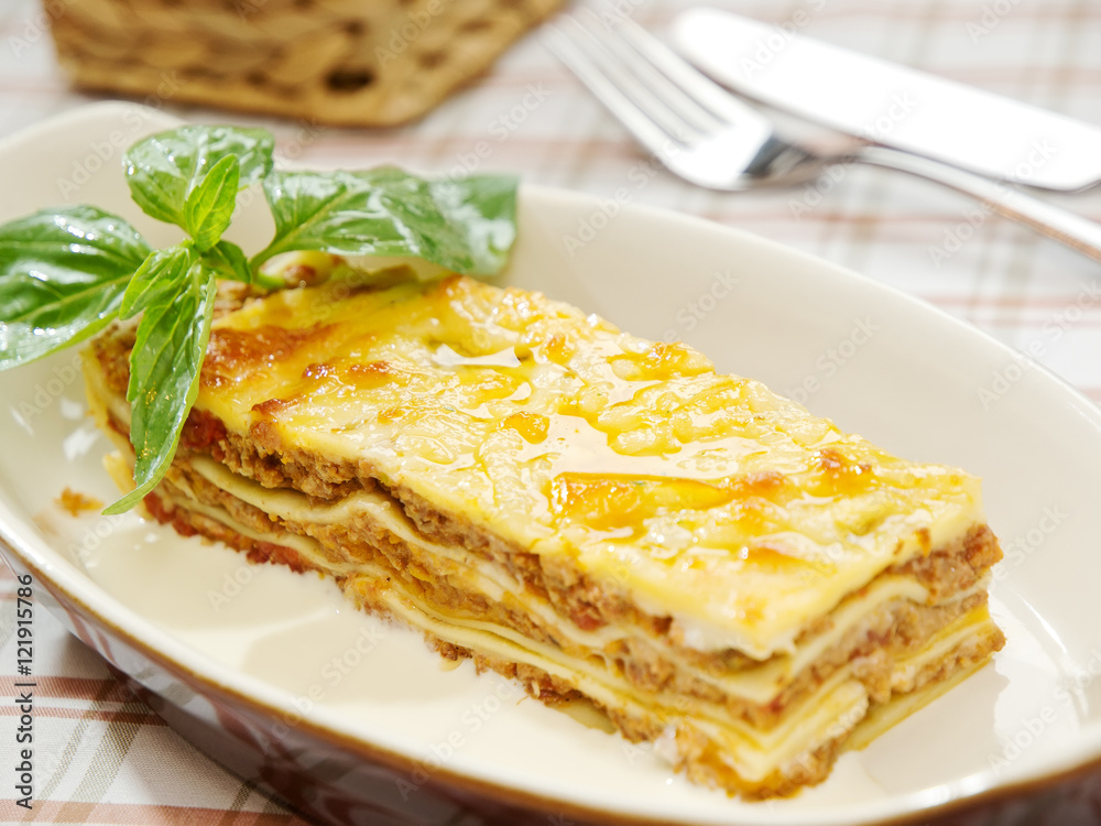 traditional lasagna made with minced beef bolognese sauce topped with basil leafs served on a white plate