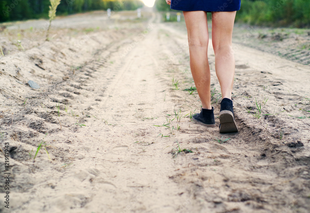 Female legs in blue boots on the sandy dusty road leaving afar in summer day Female legs in blue boots on the sandy dusty road leaving afar in summer day