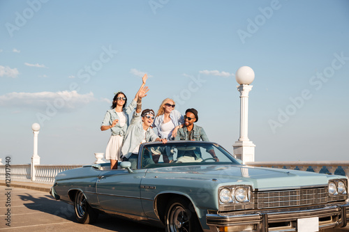Smiling young people driving old vintage cabriolet car