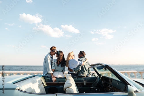 Back view of two couples standing and hugging near car