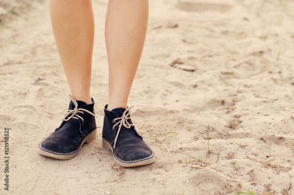 Female legs in blue boots on the sandy dusty road in summer day