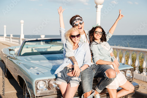 Cheerful young man and two women standing with raised hands