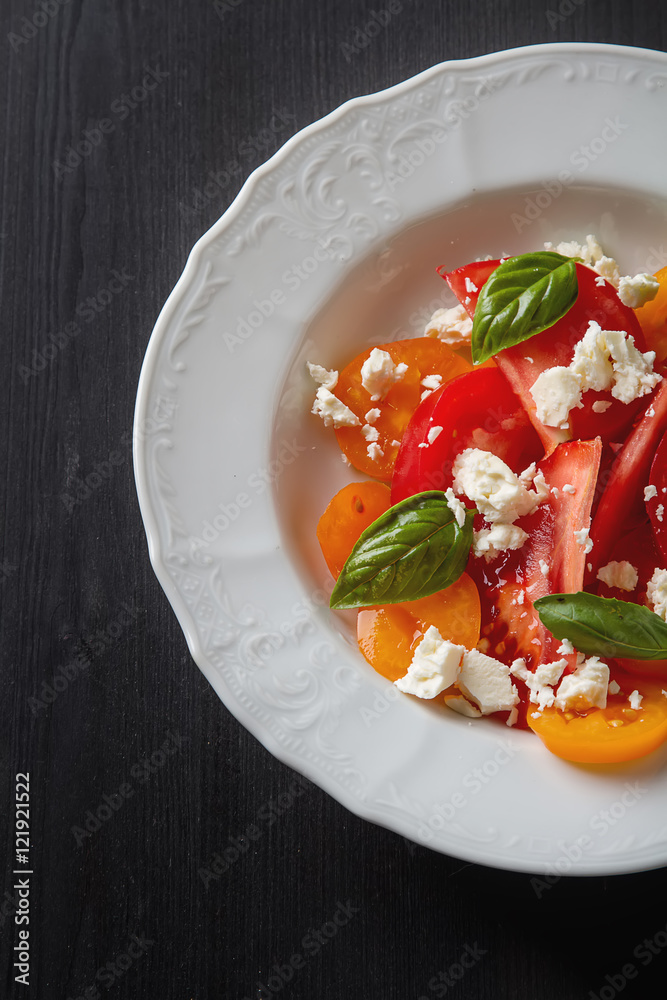 Salad of ripe tomatoes with basil and feta cheese on white teral