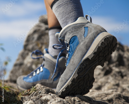 Close up of hiking boots and legs climbing up rocky trail and reaching the top of a mountain