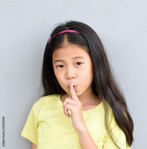 Silence gesture concept with young Asian girl with black hair and single eyelids holding finger on lips and shushing 