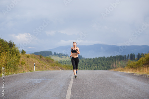Young slim woman in sportswear jogging on the road