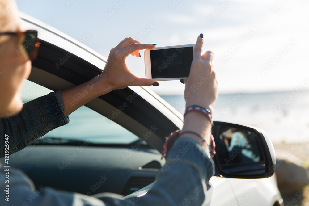 happy young woman in car with smartphone at sea