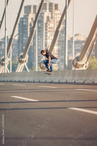 Skater doing tricks and jumping on the street highway bridge, through urban traffic. Free riding skateboard