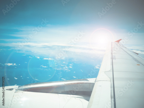 Lens flare and view of jet plane wing with cloud patterns