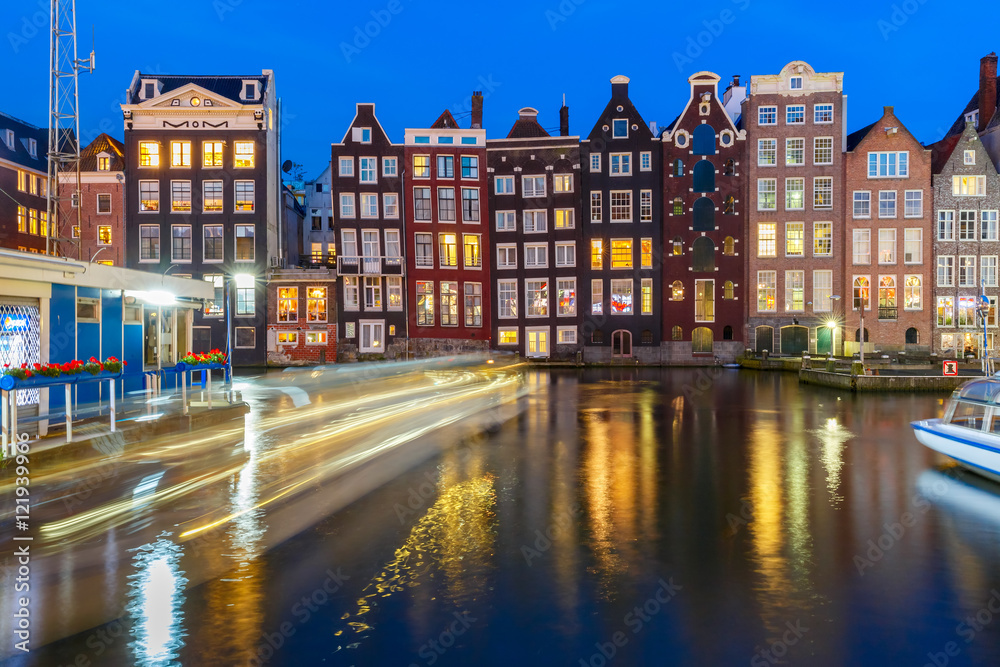 Beautiful typical Dutch dancing houses and tourist boats at the Amsterdam canal Damrak at night, Holland, Netherlands.