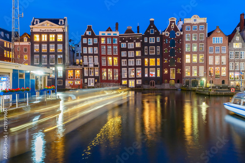 Beautiful typical Dutch dancing houses and tourist boats at the Amsterdam canal Damrak at night  Holland  Netherlands.