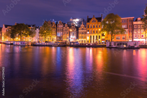 Amsterdam canal Amstel with typical dutch houses and houseboats with multi-colored reflections at night, Holland, Netherlands.