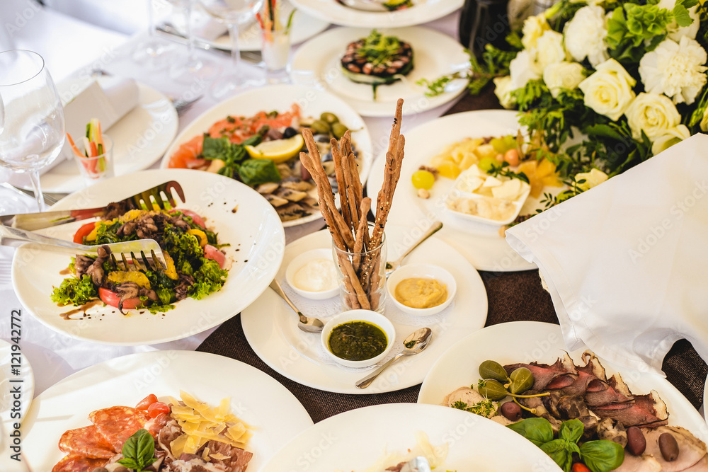 Table served with different food and flatware for dinner. Close up of many snacks, appetizers and salads on table waiting for guests. Wedding reception or family event diner in expensive restaurant.