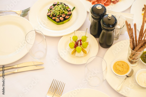 Table served with different food and flatware for dinner. Close up of many snacks, appetizers and salads on table waiting for guests. Wedding reception or family event diner in expensive restaurant.