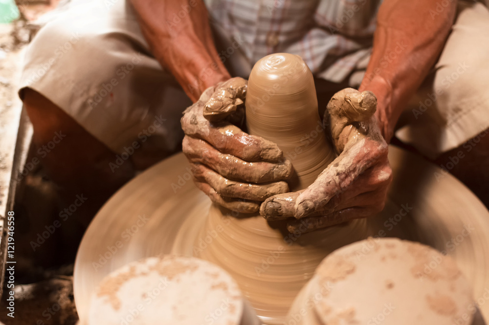 Potter hands making in clay on pottery wheel.