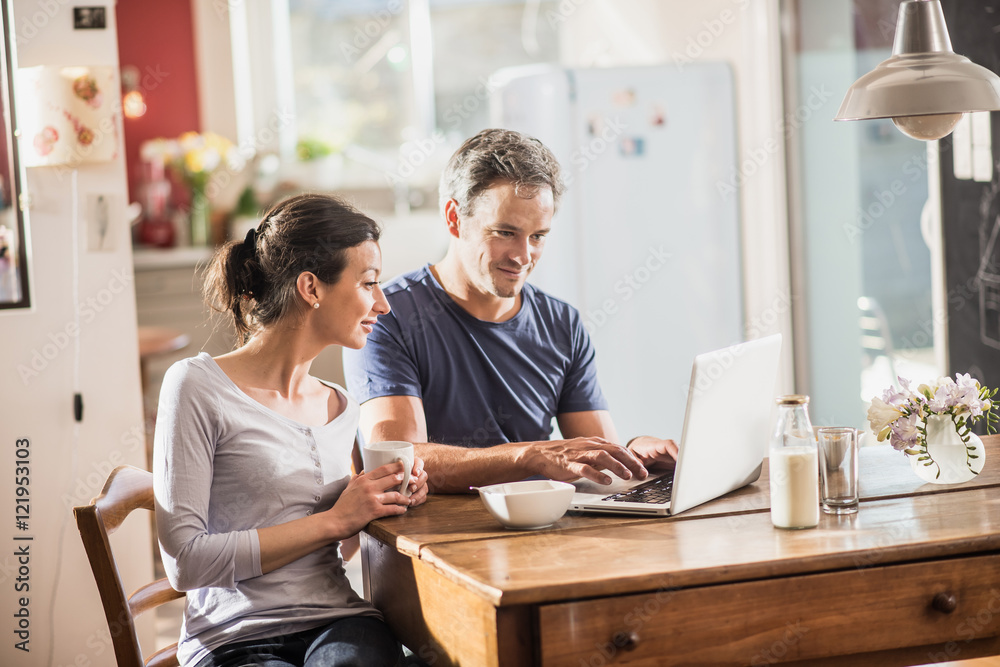 A couple using a laptop while having breakfast in the kitchen A couple using a laptop while having breakfast in the kitchen