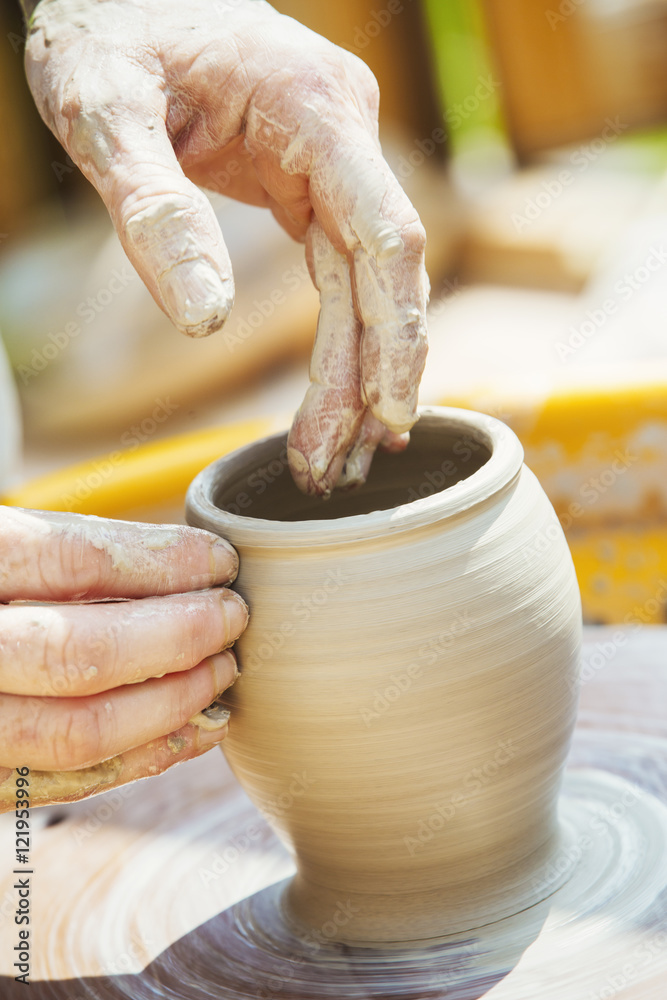 A woman potter working clay on a potter's wheel in her workshop. A woman potter working clay on a potter's wheel in her workshop.