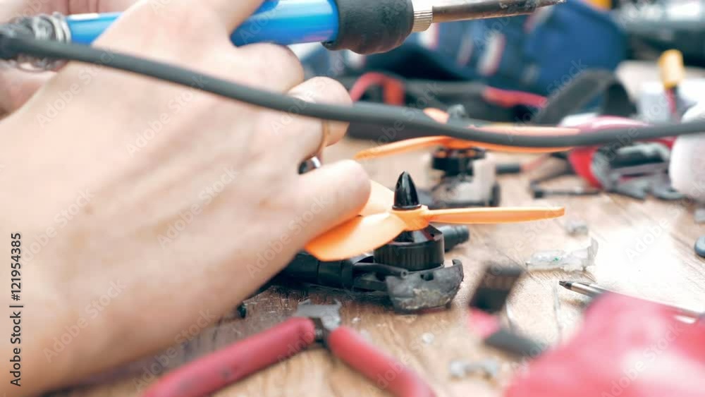 Close up of man's hands welding details while assembling FPV drone using tools, preparing quadcopter for flight. Repair drone before training process. Close up of man's hands welding details while assembling FPV drone using tools, preparing quadcopter for flight. Repair drone before training process.
