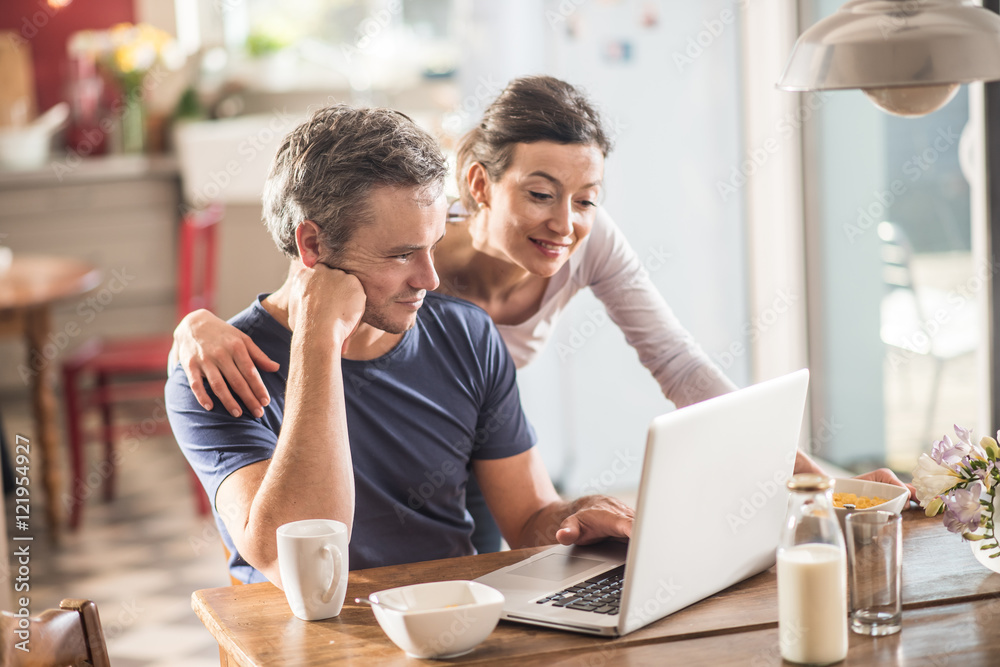 A couple using a laptop while having breakfast in the kitchen A couple using a laptop while having breakfast in the kitchen
