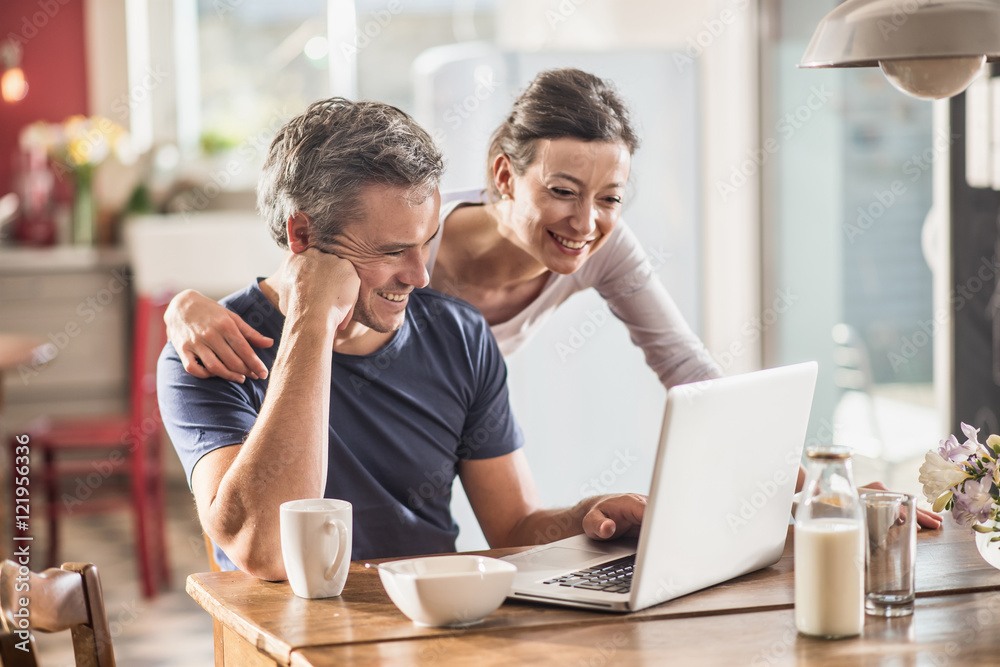 A couple using a laptop while having breakfast in the kitchen A couple using a laptop while having breakfast in the kitchen