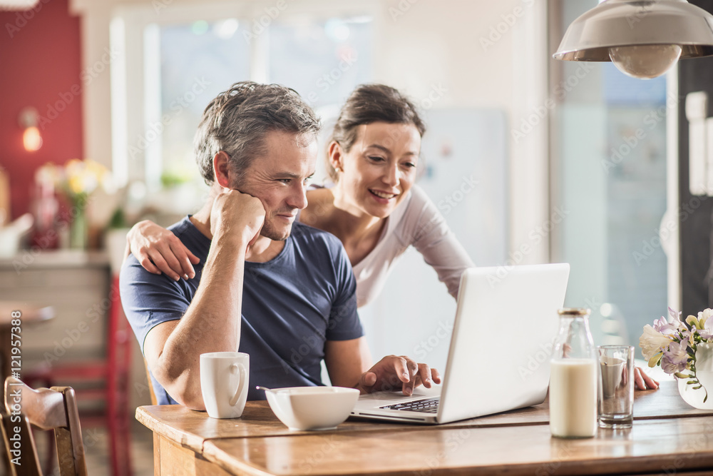 A couple using a laptop while having breakfast in the kitchen A couple using a laptop while having breakfast in the kitchen