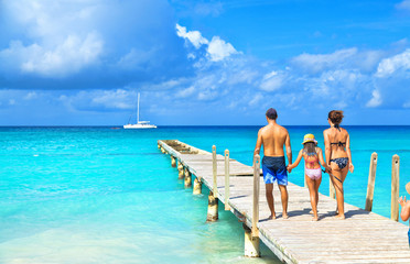 Fototapete Karibik Rückansicht einer glücklichen Familie am tropischen Strand. Familie, die auf einem hölzernen Pier steht.  © Vladimir Sazonov