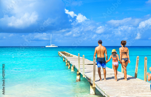 Obraz na płótnie Back view of a happy family on tropical beach. Family standing on a wooden pier. w salonie