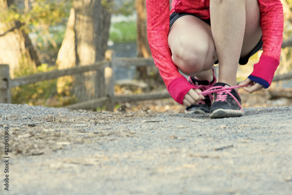Female runner tying shoe on an outdoor path Female runner tying shoe on an outdoor path