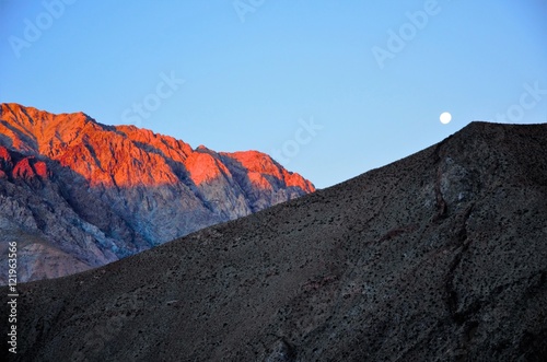 Bright moon in the blue sky behind hills with the little village Pisco Elqui in the foreground in Chile, South America