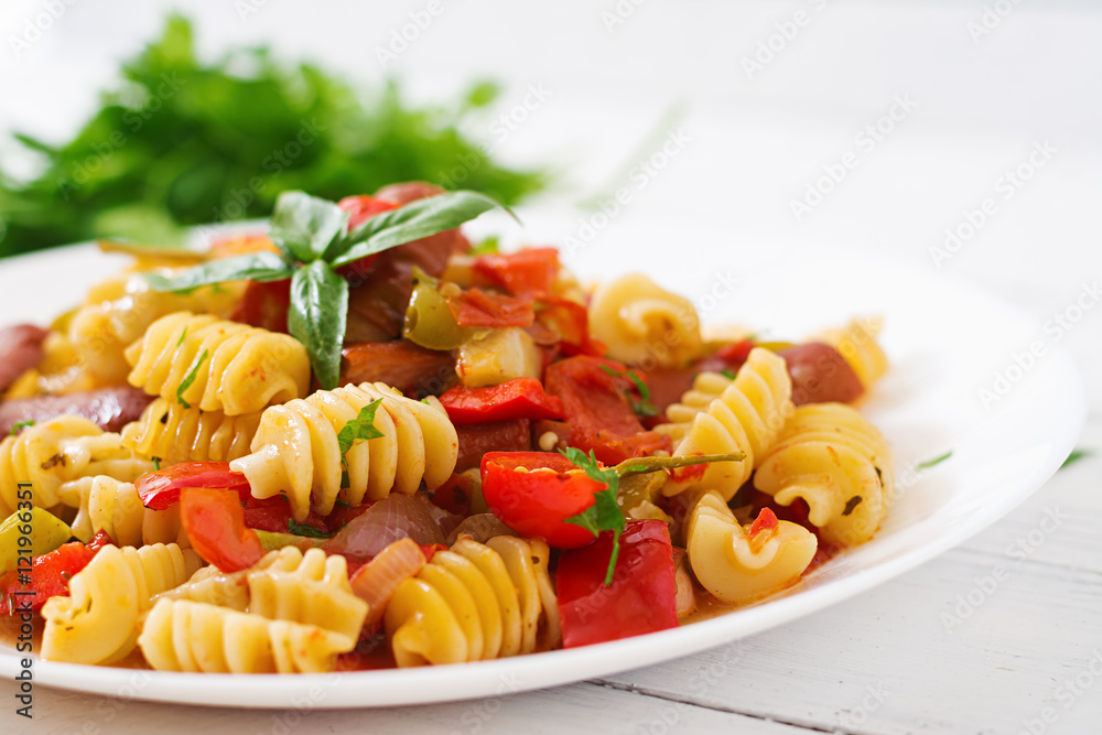 Pasta with tomato sauce with sausage, tomatoes, green basil decorated in white plate on a wooden background.
