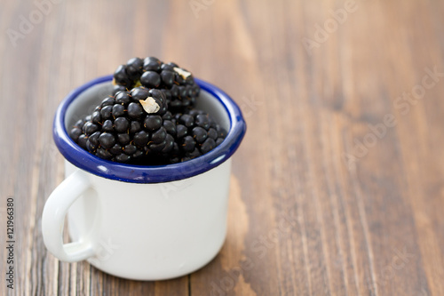 blackberries in white cup on brown .wooden background