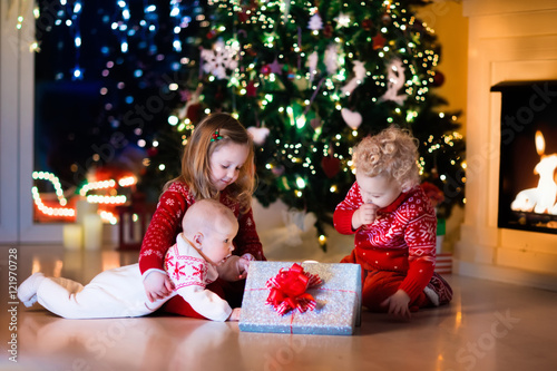 Kids opening Christmas presents at fireplace © famveldman
