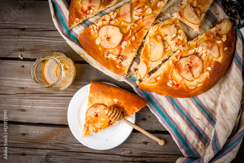 Freshly prepared fruit focaccia cake with pears and almonds on a rustic table with a towel, close - honey for pouring