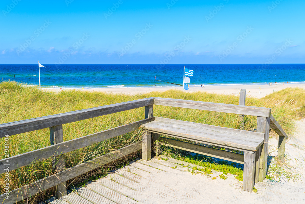 Fototapeta premium Drewniana ławka przy wejściem piaskowata plaża w Kampen wiosce na Sylt wyspie, Niemcy