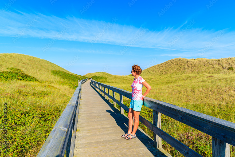 Young woman tourist standing on wooden walkway to beach among sand dunes on Sylt island, Germany