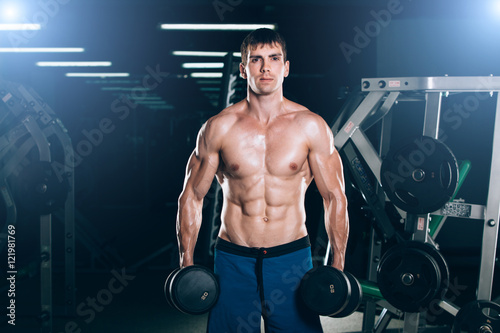 sport, fitness, lifestyle and people concept - Muscular bodybuilder guy doing exercises with dumbbells in gym