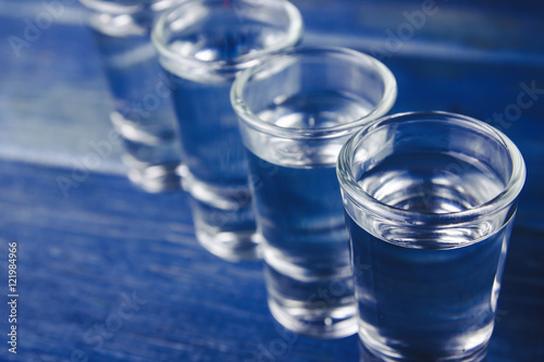 Vodka shots filled with alcohol on wooden blue bar.