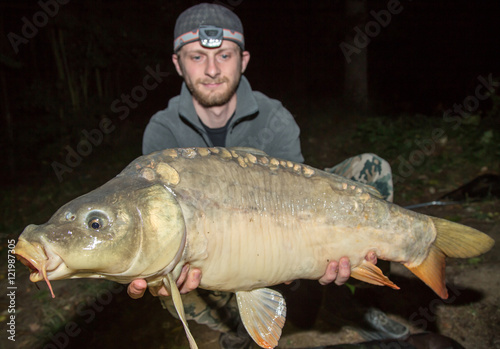 Fototapeta Naklejka Na Ścianę i Meble -  Happy angler with carp fishing trophy. Night fishing.