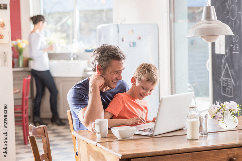  Cheerful father and son using a laptop while having breakfast - obrazy, fototapety, plakaty 