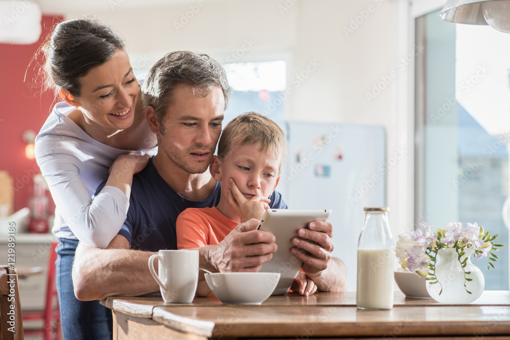 A family using a tablet while having breakfast in the kitchen A family using a tablet while having breakfast in the kitchen
