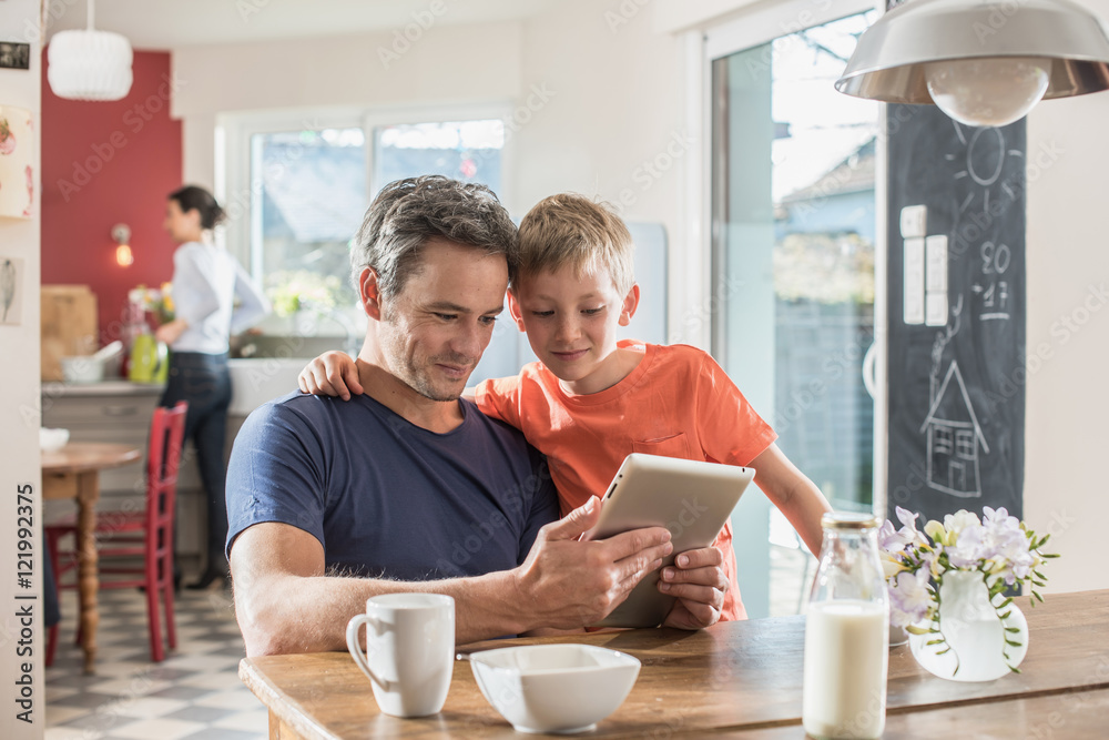 A father and son using a tablet while having breakfast A father and son using a tablet while having breakfast