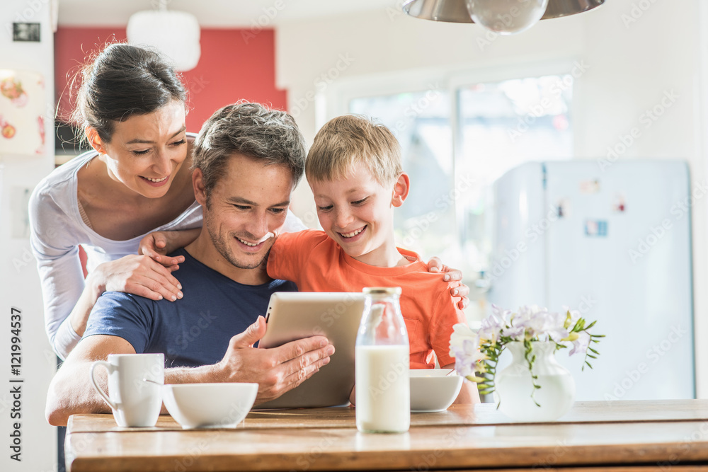A family using a tablet while having breakfast in the kitchen A family using a tablet while having breakfast in the kitchen