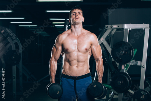 sport, fitness, lifestyle and people concept - Muscular bodybuilder guy doing exercises with dumbbells in gym.