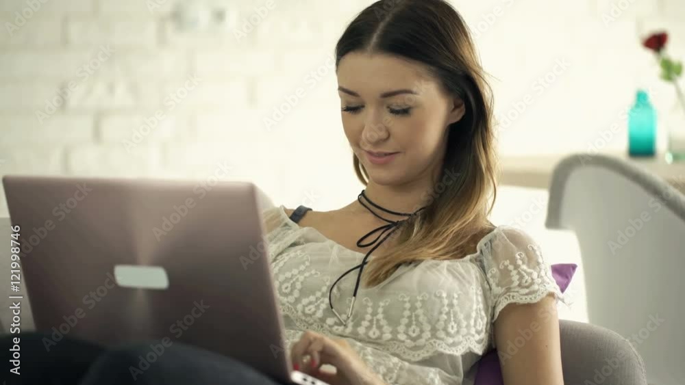 Young, pretty woman using laptop sitting on armchair at home
